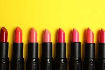 Fototapeta premium Many bright lipsticks on yellow background, flat lay. Space for text