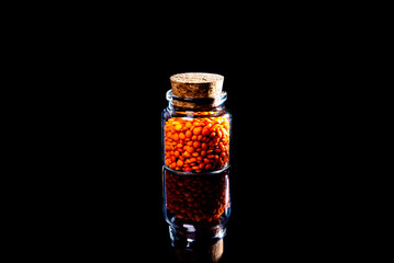 Close up of Raw Masur dal or masoor lentils or pink lentils in a black colored clay bowl on black in wineglass glass jar bucket