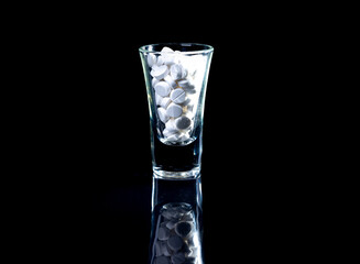 white orange pills in wineglass glass . in jar. in bucket Isolated on black set of capsule and pills inside closeup,