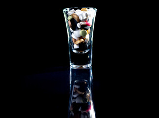 white orange pills in wineglass glass . in jar. in bucket Isolated on black set of capsule and pills inside closeup,