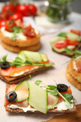 Tasty rye crispbreads with salmon, cream cheese and vegetables on wooden board. closeup