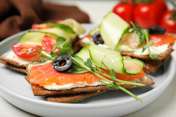 Tasty rye crispbreads with salmon, cream cheese and cucumber on plate, closeup