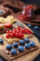 Fresh crunchy rye crispbreads with different toppings on wooden board, closeup