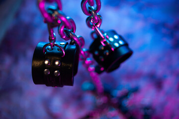 BDSM toys leather handcuffs on a metal chain and neon light