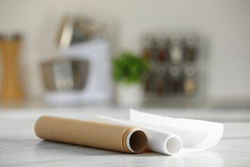 Rolls of baking paper on white marble table against blurred background indoors. Space for text