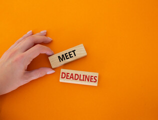 Meet Deadlines symbol. Concept word Meet Deadlines on wooden blocks. Businessman hand. Beautiful orange background. Business and Meet Deadlines concept. Copy space