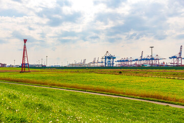 Fototapeta na wymiar Industrial area cranes red tower lighthouse dyke seascape panorama Germany.