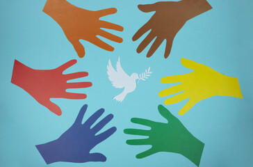 Multicolored paper hands reach for a paper pigeon on a blue background. World Peace Day. World Science Day for Peace and Development