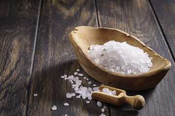 Coarse salt with scoop in wooden bowl on oak table