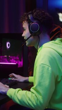A teenager plays computer games while sitting in front of a monitor with a green screen