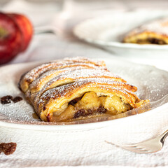 Homemade apple strudel with puff pastry, cinnamon, sultanas, pine nuts on white plate. Christmas apple strudel.