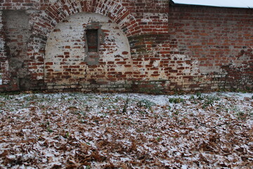 Red brick wall and yellow leaves on the ground in snow