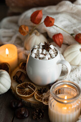 Obraz na płótnie Canvas Autumn cozy home composition with hot chocolate with marshmallow and candles. Aromatherapy on a grey fall morning, atmosphere of cosiness and relax. Wooden background, window sill, close up.