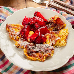 Closeup of Kaiserschmarrn scrambled pancake sprinkled with powdered sugar and caramelized plums