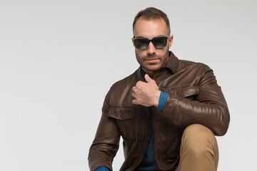 casual man is squatting and wearing a brown leather jacket