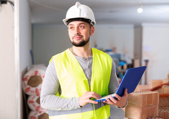 Civil engineer working on a construction site indoors monitors the process of capital repairs of a brick house on a laptop