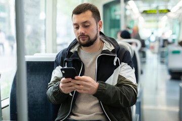 Portrait of positive bearded guy traveling in city bus and using mobile phone..