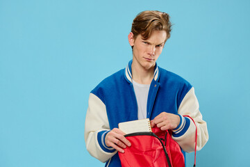 a young student in a bomber jacket takes out a notebook from his backpack looking at the camera