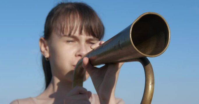Teenager with mountain. Teen girl blowing into the bugle against the blue sky.