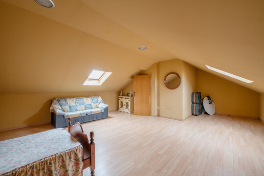 Attic Bedroom Of Single Family Home With Small Wooden Bed And Ugly Sofa Under Skylight, Hardwood Floor And Round Wood Framed Mirror