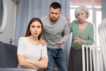 Stressed young woman sitting at home while her male and mature female relatives scolding her