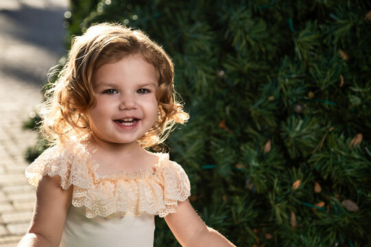 Smiling little girl with brown, blonde hair and white outfit and stroller