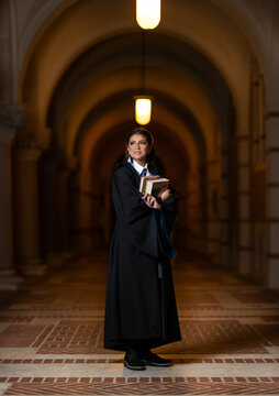 School girl in university hall wearing black robe and holding books with magic wand