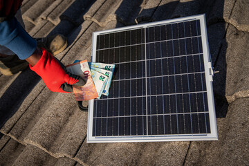 A worker installs a sun brush and holds money in his hand, energy crisis in Europe.
