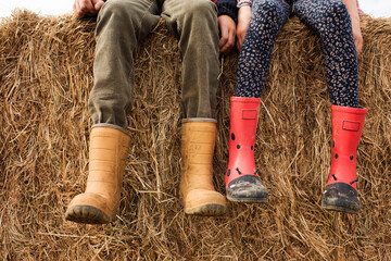 two children's feet and rain boots on a hay bale