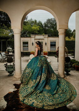 girl in an emerald green and gold wedding dress posing under arches 