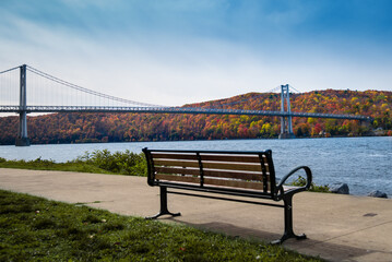 An Autumn view of the mid-Hudson bridge in New York state with a empty bench in the foreground. 