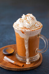 Pumpkin Spice Coffee Latte topped with whipped cream and cinnamon overflowing in a clear glass mug; copy space