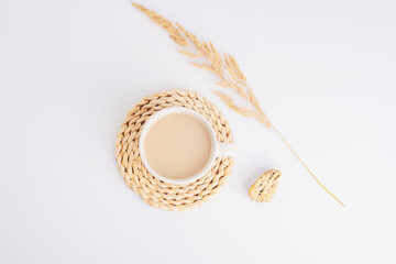 Coffee or cocoa cup on a wicker coaster and pampas grass on white background. Still life. Top view,...