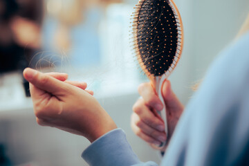 Woman Cleaning a Hairbrush Suffering from Hair Loss. Girl having her hair falling out from alopecia...