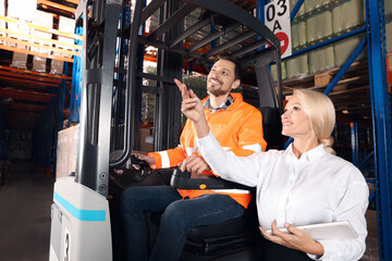 Happy worker talking with manager while sitting in forklift truck at warehouse