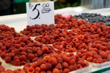 Cartons of Berries at the Farmers Market. Small boxes with raspberries displayed on food market, closeup detail. Red raspberries in baskets on a stand at a farmers market.