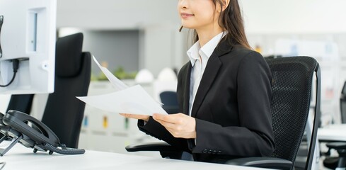資料とパソコンを見る若いスーツを着た日本人女性