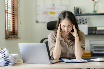 Fototapeta na wymiar Asian businesswoman headache during work analyzing financial graphs with laptop at her desk stressed woman Headache during overtime at home office