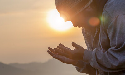 Human with hands open palm up praying to God on the mountain sunset background.