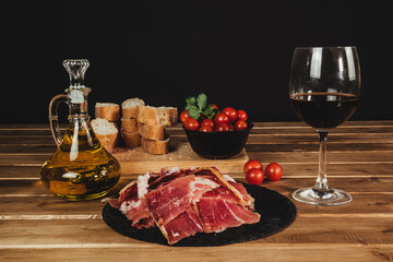 delicious plate of Iberian ham accompanied by tomatoes, olive oil, bread and a glass of Spanish red...