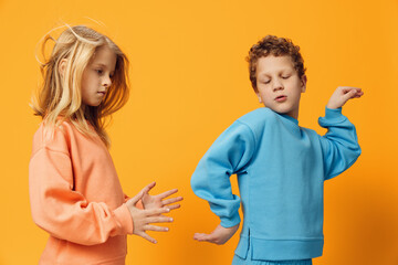 cute, beautiful children, brother and sister stand on a yellow background in bright clothes and pose funny dancing. Horizontal studio photography
