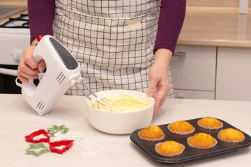 Caucasain woman making cream for decorating freshly made cupcakes or maffins at the kitchen