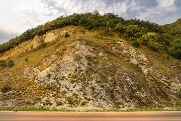 A rocky dry yellow cliff, descending down, against the background of a blue cloudy sky. Autumn...