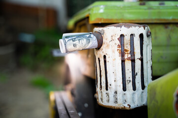 A hundred dollar bill covers the exhaust pipe of a mini tractor. Money and the agricultural...