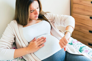 Pregnant pain contractions. Pregnant woman watching clock, holding baby belly. Childbirth time, contractions pain. Pregnancy, medicine health care concept.