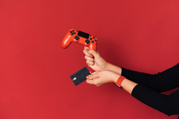Gamepad and credit card in female hand against red background. © Anastassiya 