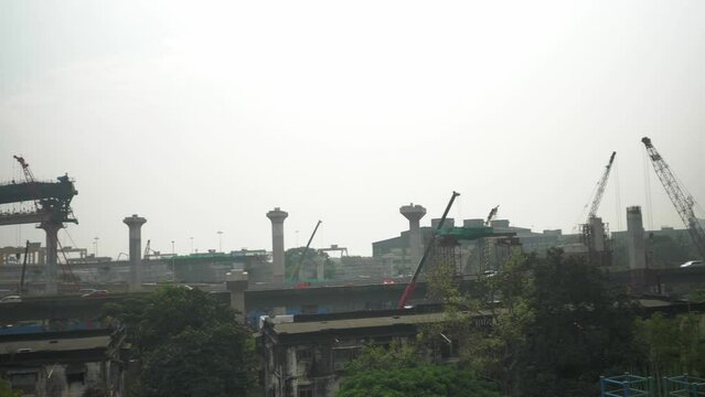 Pan right shot of Wadala metro construction site with heavy machines and cranes around, cars crossing each other on city flyover, Mumbai