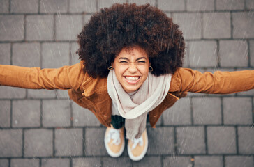 Black woman, stand to feel rain and happy in city in winter with smile, afro or trendy fashion....