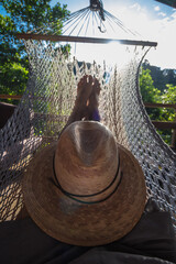 adult man lying in a hammock with a hat on a sunny morning - obrazy, fototapety, plakaty