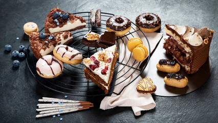 Table with various cookies, donuts, cakes, cheesecakes on dark background.